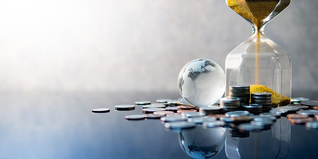 Golden hourglass, coins and glass globe on desk