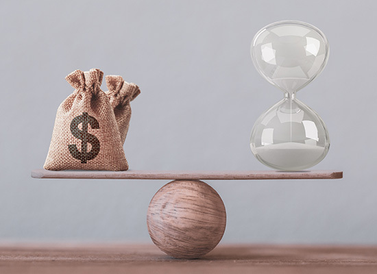 money and an hour glass on a board balancing on a ball