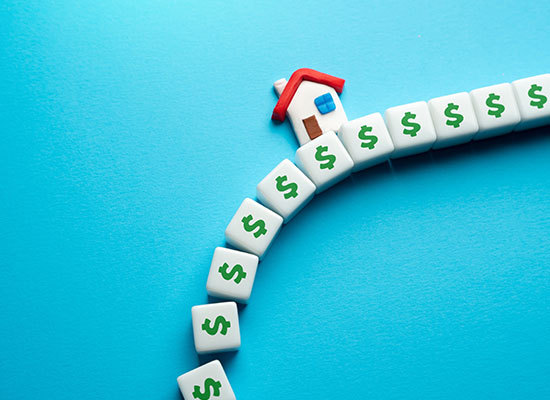 stylized image showing a house falling off a block of bricks that have dollar signs on them