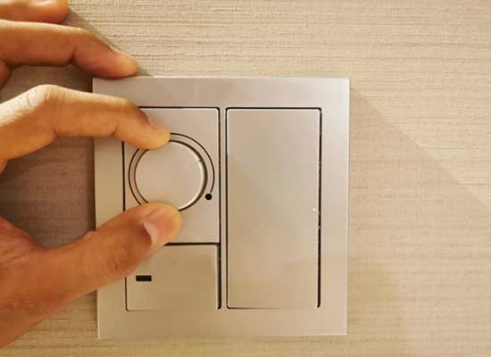  A hand adjusts a modern, circular dimmer switch next to a rectangular light switch on a textured wall, much like a dimmer switch adjusts light, an Indexed Universal Life insurance policy lets you fine-tune your financial glow, balancing risk and return.