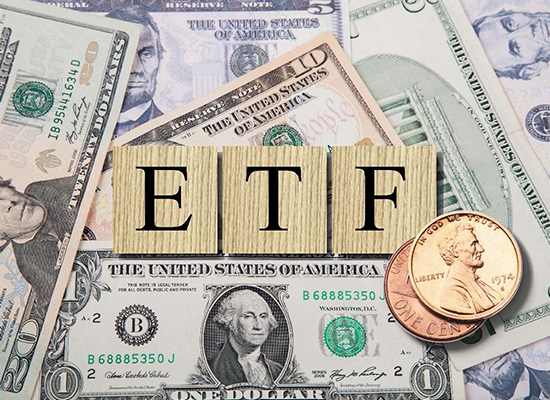 The letters 'ETF' spelled out with wooden blocks across a spread of US dollar bills, including a one-dollar and twenty-dollar note, with a penny resting near the letter 'F'