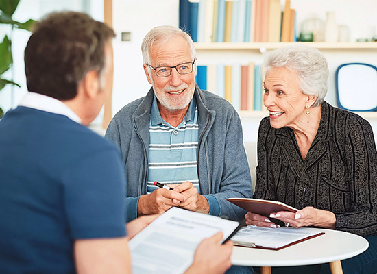 An elderly couple smiles while discussing financial documents with a financial advisor, highlighting retirement planning and financial preparedness.