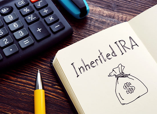 A notebook open to a page with 'Inherited IRA' written in bold letters next to a drawing of a money bag with a dollar sign. Beside the notebook, there is a calculator, a yellow pen, and a blue highlighter on the wooden surface—an essential scene for anyone diving into estate planning under the SECURE Act.