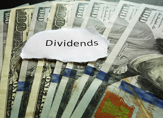 A pile of hundred-dollar bills with a torn paper labeled Dividends,' illustrating financial planning and the role of dividends in investment strategies.