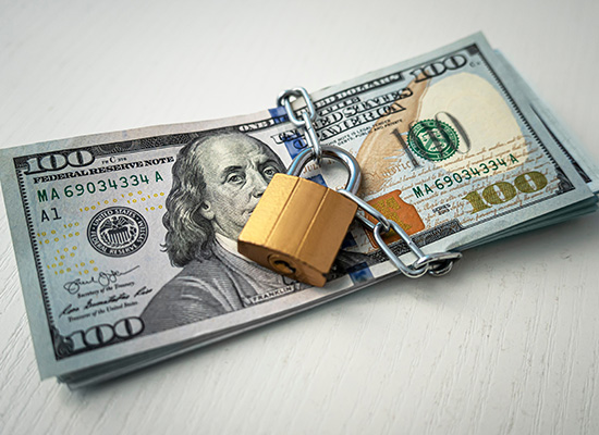 A stack of $100 bills is secured with a padlock and chain, representing financial security and protection.