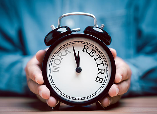 A person in a blue shirt holds an alarm clock. The clock's face is divided into two halves, labeled 'WORK' on the left and 'RETIRE' on the right. The hands point towards 'RETIRE,' hinting at transitioning to retirement, much like a Roth IRA conversion signifies planning for one's future financial freedom.