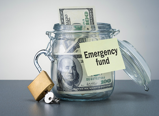 A jar labeled 'Emergency fund' is filled with U.S. dollar bills, secured with a padlock, representing financial planning and savings.