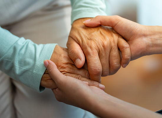A younger person holds the hand of an elderly individual, symbolizing caregiving, emotional support, and the challenges of caring for aging parents.