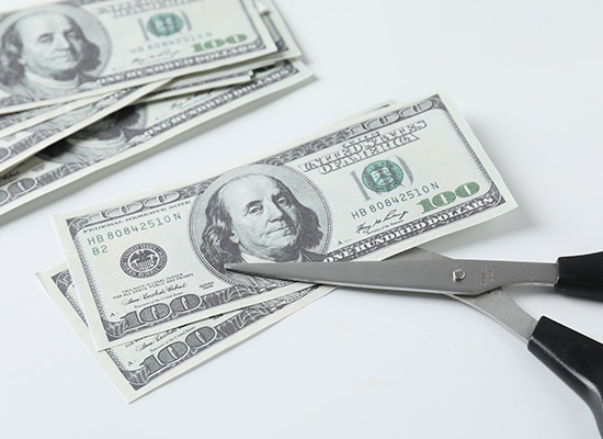 Scissors cutting a hundred-dollar bill, illustrating the financial challenges caregivers encounter when planning for retirement.