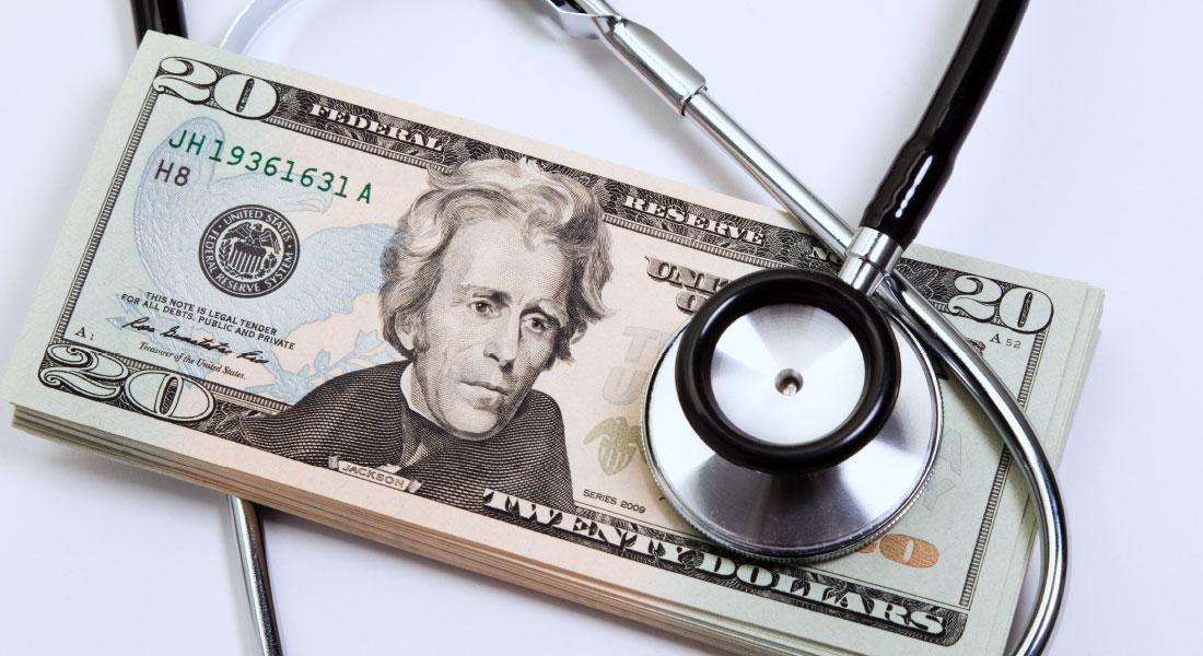 A stethoscope resting ontop of a stack of twenty dollar bills