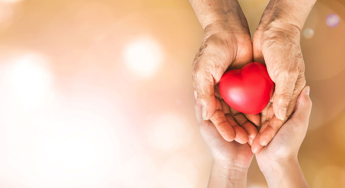 A small child's hands under their grandparent's hands holding a heart together with compassion.