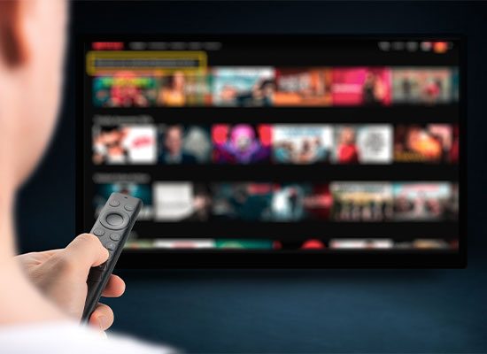 A person holding a remote control and browsing through a selection of movies on a blurred smart tv screen
