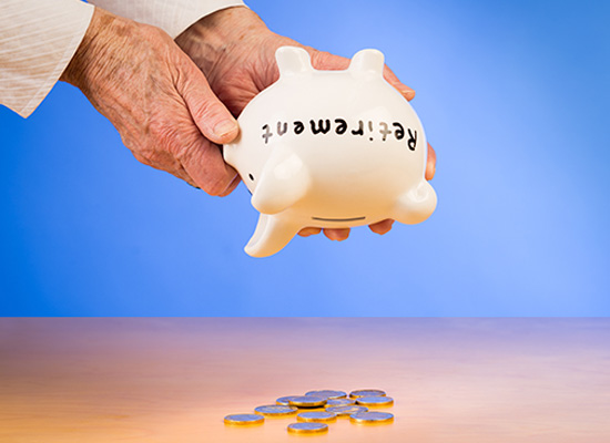 A hand holding an upside-down piggy bank with the word 'Retirement' on it, shaking out the last few coins onto a table.