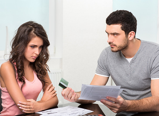 A young couple looking concerned while discussing finances with credit card and bills on the table.