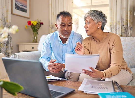 An older couple reviews financial documents together on a laptop, illustrating retirement planning and financial strategy discussions.