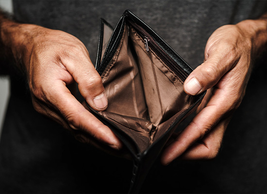 Hands holding an open, empty black wallet reveal its brown interior against a dark background
