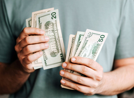 A person wearing a green shirt is focused on retirement planning, holding and counting several U.S. dollar bills