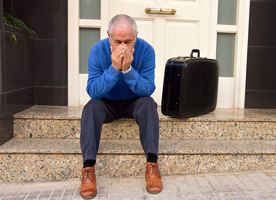 An elderly man sits on the steps with his suitcase, looking distressed, symbolizing financial challenges and difficult transitions in later life.