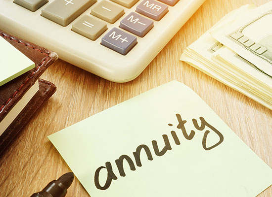 A desk with a calculator, cash, and a sticky note labeled 'annuity,' representing financial planning strategies for long-term care and retirement.