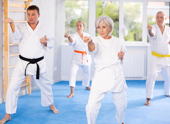 Four senior adults in karate uniforms practicing martial arts in a bright, spacious dojo. they are in various stances, demonstrating focus and determination.