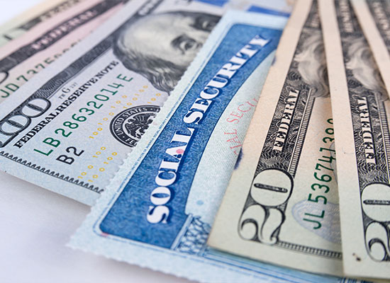 A close-up of a U.S. Social Security card and various denominations of U.S. dollar bills, including $100, $20, and $10 bills, spread out on a surface. The image suggests themes of finance, social security, retirement planning, and money management.