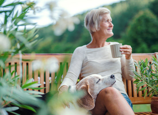 A woman with short hair sits on a wooden bench outdoors, holding a mug, contemplating the gender gap as her beagle rests its head on her lap
