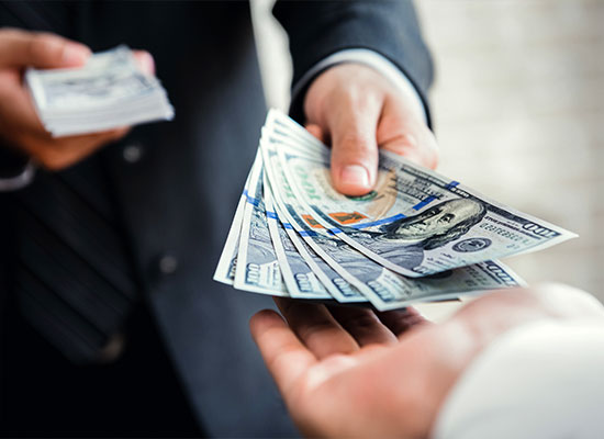 A financial professional in a suit hands over a stack of hundred-dollar bills to another person, who eagerly reaches out to receive them. 