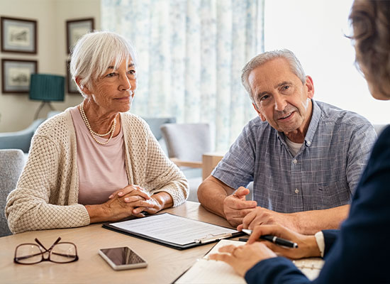 An elderly couple is sitting at a table, deep in conversation with a financial professional.