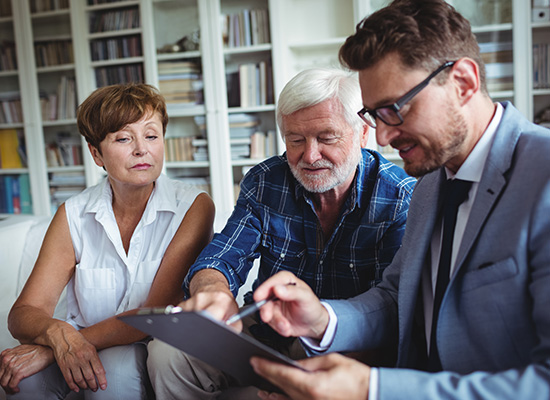  In a home library setting, a financial advisor or wealth management professional reviews documents with a mature couple during what appears to be a retirement planning consultation.