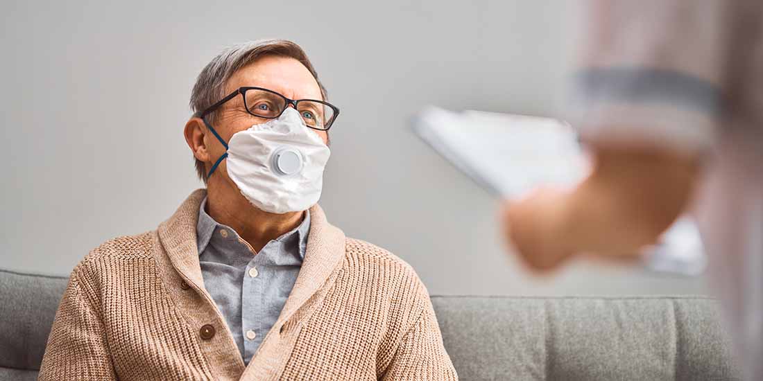 A senior man wearing a mask talking to his doctor