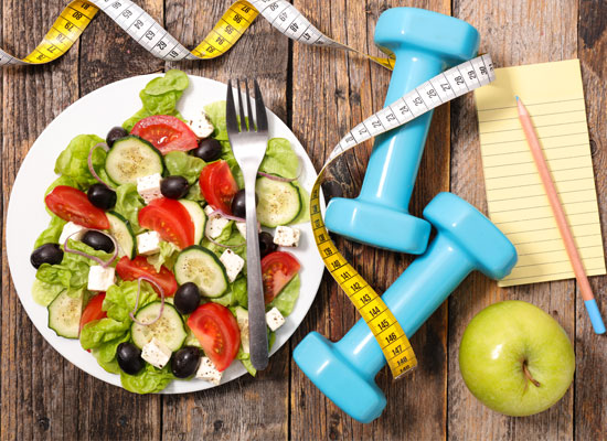 A salad, apple, weights, measuring tape, pencil and a notepad on a table