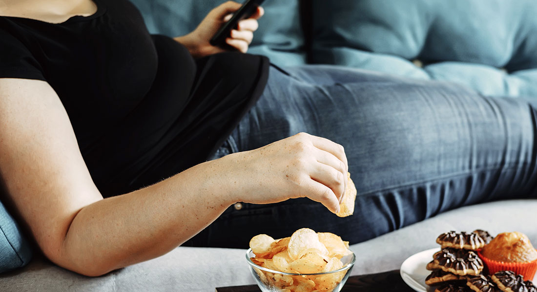 Woman sitting on the couch with potato chips and a tray of baked goods.