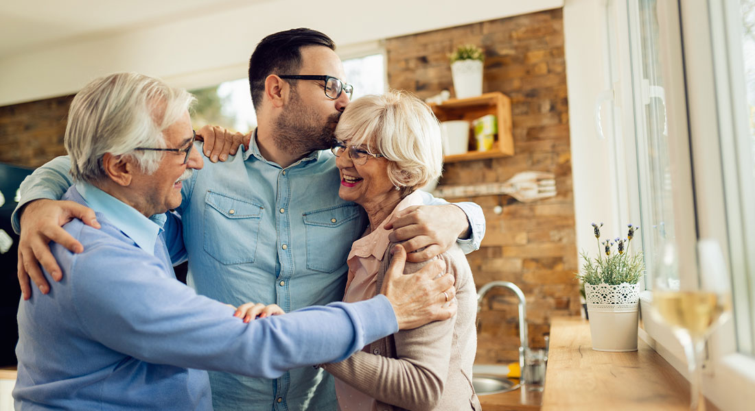 A son hugging his smiling parents as they are happy about him managing the parents health care