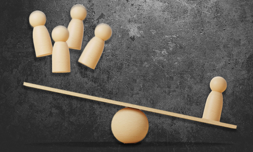 Wooden figures arranged in a seesaw balance concept, with three figures on one side and one on the other, mirrors the delicate balancing act of the American health system, where the weight of one's decisions can tip the scales of fate in unexpected ways.