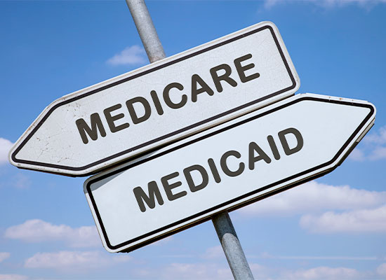 Two street sign arrows pointing in opposite directions against a clear blue sky, one labeled 'MEDICARE' and the other labeled 'MEDICAID,' guiding you through retirement health insurance choices.