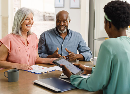 A cheerful couple discusses long-term care insurance options with a financial advisor to secure their health care needs during retirement.