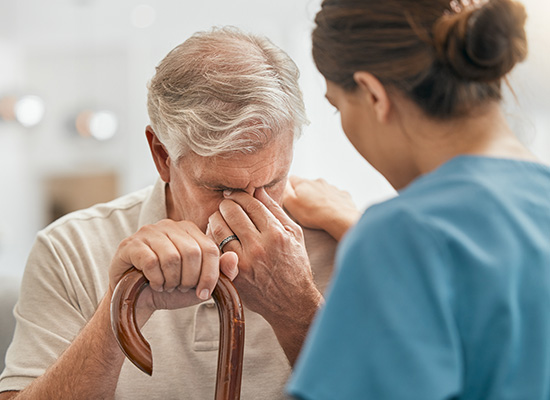 An elderly man with a cane being comforted by a caregiver, depicting the aging population and the importance of long-term care.