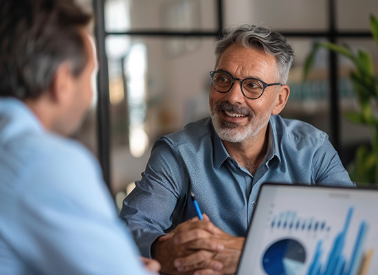 A smiling older man in a business meeting, discussing financial planning, possibly related to retirement age and strategies to manage health care coverage under Medicare.