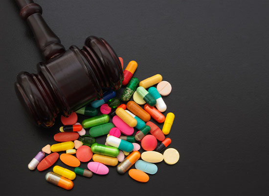 A wooden gavel rests on a pile of various multi-colored pills and capsules against a dark background. The image symbolizes the intersection of law and prescription medication.