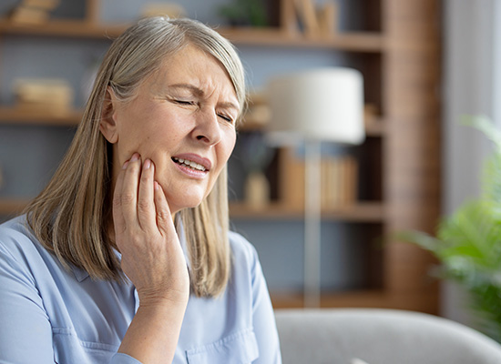 An elderly woman experiencing tooth pain, emphasizing the impact of inadequate dental care on senior health.