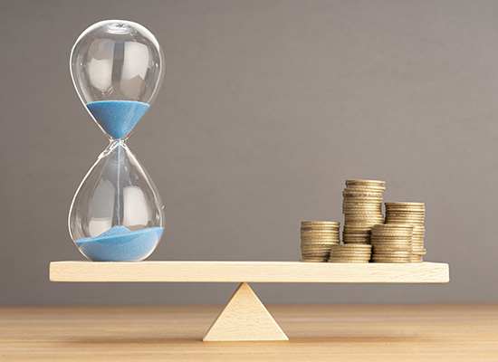 An hourglass balanced with coins symbolizes the importance of managing time and finances for health care planning in retirement.