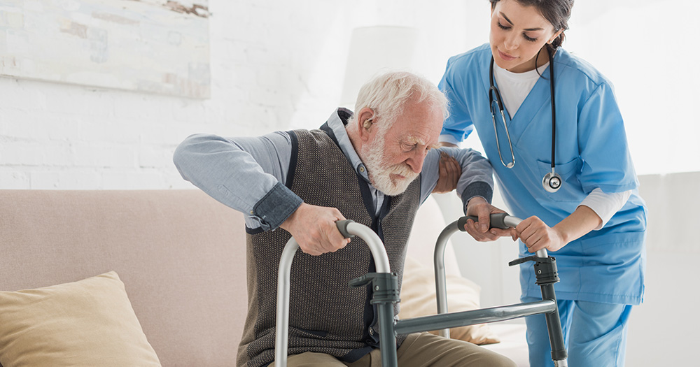 In home nurse helping a gentleman stand up using his walker