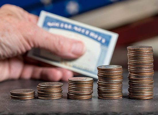 coins stacked in iterations going up on a table and a social security card in a persons hand
