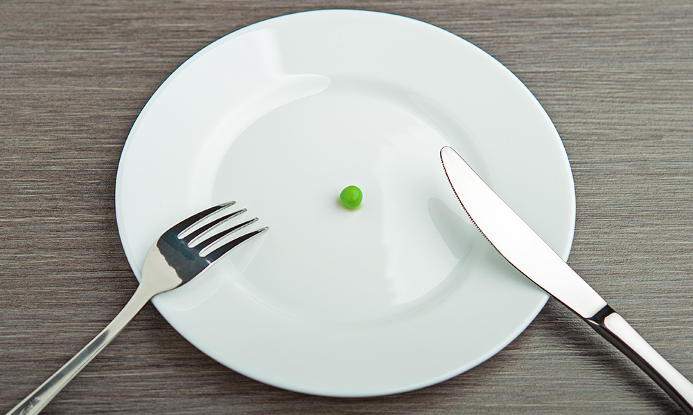 a plate with a single green pea, fork and knife on it