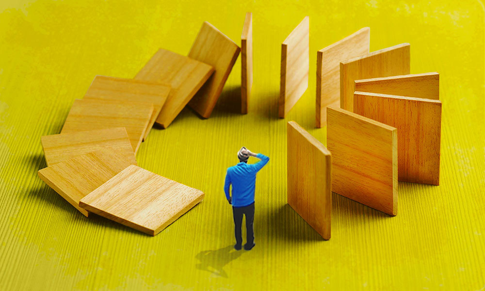 Person looking confused at wooden tiles toppling over like dominoes