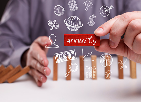 A person's hand inserting a block labeled 'annuity' into a series of dominoes with various financial symbols drawn above them, illustrating the strategic placement of annuities within financial planning.