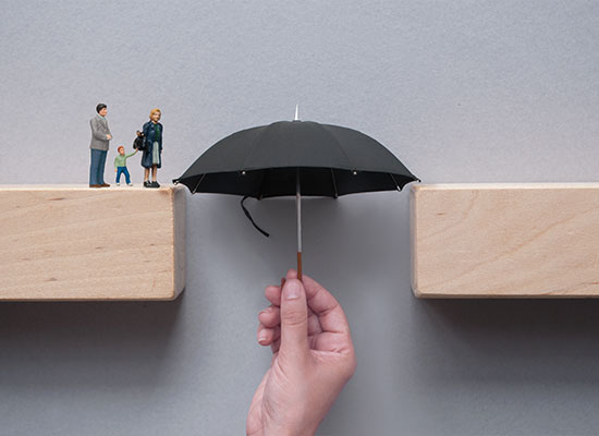 A creative setup showing a hand holding a black umbrella serving as a bridge between two wooden blocks, where miniature figures of a family are crossing.