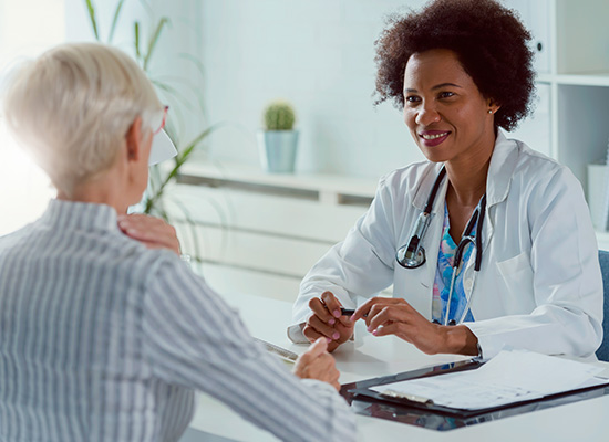 A female doctor with a stethoscope around her neck consulting an elderly female patient in a bright medical office.