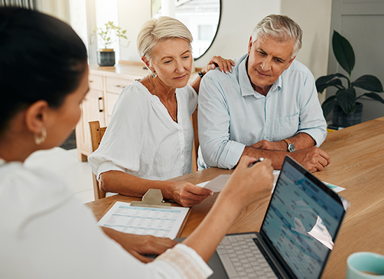 Senior couple consults with a financial advisor at a table with documents and a laptop, focused and engaged in discussion.