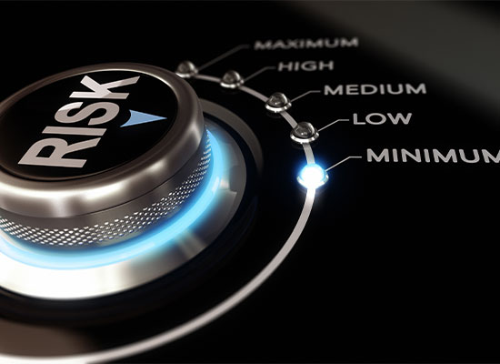 A close-up of a button labeled 'risk' with a glowing blue light, set on a panel displaying a scale with 'minimum, low, medium, high, maximum' risk levels.